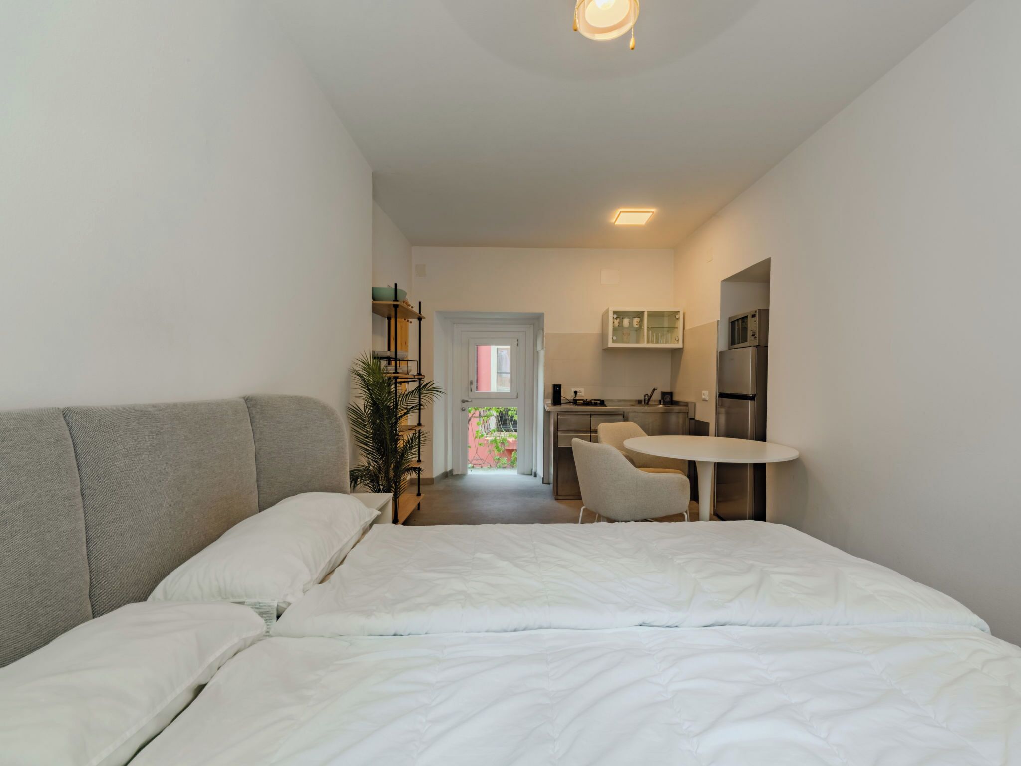 A compact hotel room with a bed, a small kitchenette, a dining table, and a view of the outside.