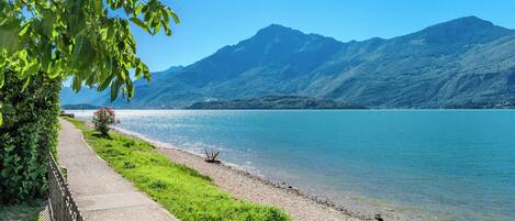 A lakeside path with a view of mountains and a clear sky.