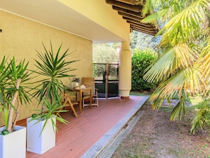 Ein überdachter Patio-Bereich mit Tisch und Stühlen, umgeben von Kübelpflanzen und Blick auf einen Garten.