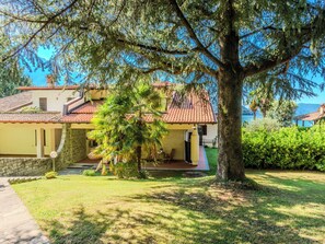 Uma casa com telhado de azulejos, parede de pedra e uma grande árvore no jardim frontal.
