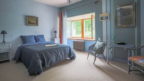 Een slaapkamer met een bed, een stoel, een bureau en een raam met gordijnen.