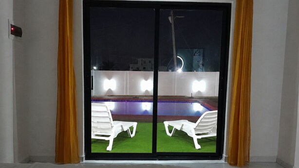 Quarto com porta de vidro deslizante que dá para área externa com piscina e duas espreguiçadeiras brancas.