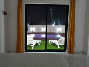 A room with a sliding glass door leading to an outdoor area with a pool and two white lounge chairs.