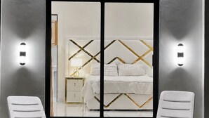 Quarto com cama, duas cadeiras brancas, uma mesinha e ar condicionado fixado na parede.