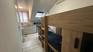 Una habitación pequeña con literas, kitchenette y tragaluz.