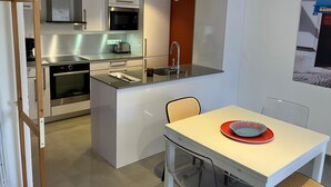 Eine moderne Küche mit Edelstahlgeräten, einer zentralen Kochinsel mit Spüle sowie einem Essbereich mit Tisch und Stühlen.