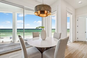 Ein stilvoller Essbereich mit einem runden Tisch, vier Stühlen, einer Vase und Blick auf den Ozean.