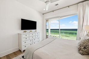 Ett sovrum med en stor säng, en platt-TV som är monterad på väggen, en byrå och ett stort fönster med utsikt över havet.