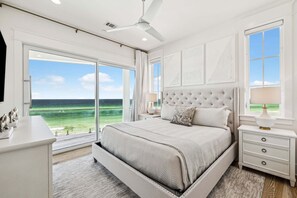 Ein Schlafzimmer mit großem Fenster, einem Bett, einem Nachttisch und einem Deckenventilator.