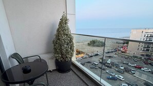 Uma varanda com vista para a praia, um vaso de planta, uma mesa e cadeiras.