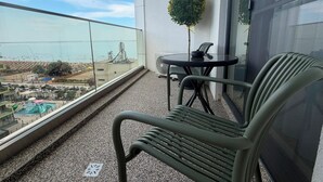Uma varanda com vista para o mar, uma pequena mesa com cadeiras e um vaso de planta.