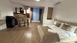 Quarto de hotel com cama, escrivaninha e cozinha compacta.