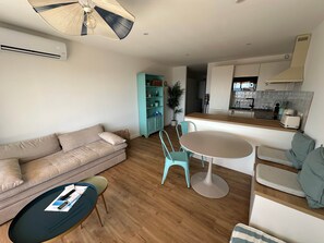A modern living room with a sofa, a coffee table, and a dining area with a table and chairs. - Fully renovated apartment with a beautiful ocean view (Sausset-les-Pins)