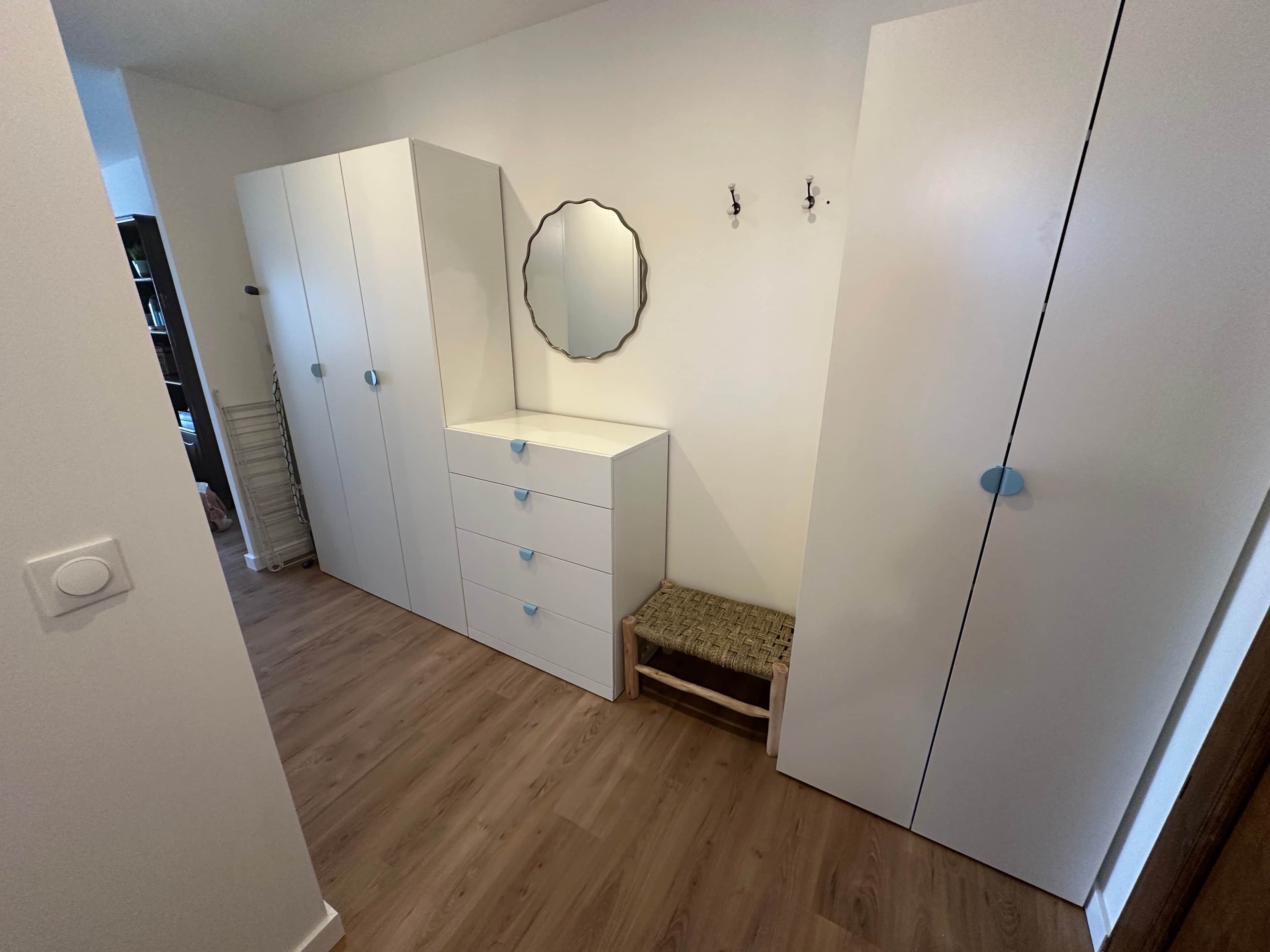 Ein Schlafzimmer mit Kleiderschrank, einer kleinen Bank, einem Spiegel und einer Wandleuchte.