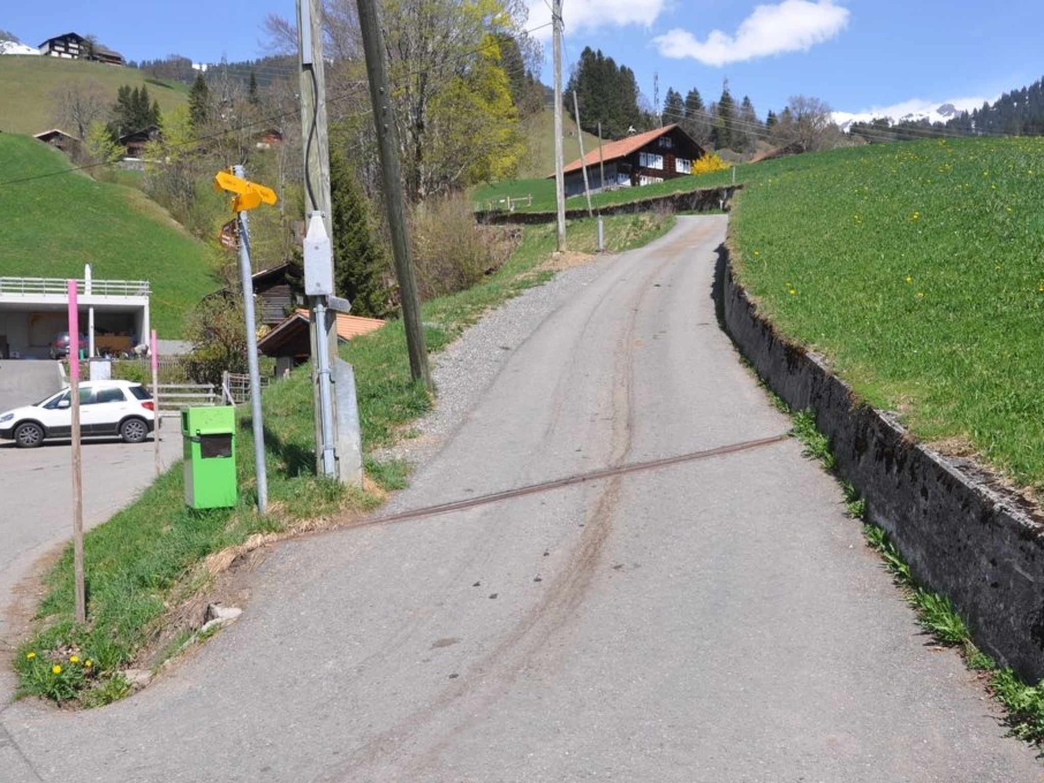 Une route de campagne avec une maison sur une colline, une voiture garée sur le bord et un coffret de raccordement vert.