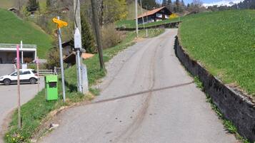 Une route de campagne avec une maison sur une colline, une voiture garée sur le bord et un coffret de raccordement vert.