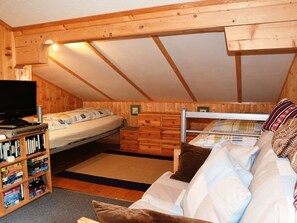 A small, cozy attic bedroom with a bunk bed, a single bed, a TV, and a bookshelf.