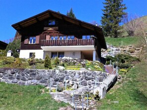 Un chalet à deux étages, doté d’un mur de soutènement en pierre et d’un escalier menant à l’entrée.