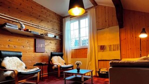 Een gezellige kamer met houten wanden, een groot raam, een bank, twee stoelen, een kleine tafel en een lamp.