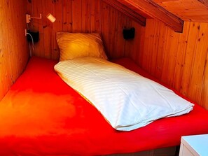 A single bed with a red mattress in a wooden room with sloped ceilings. - HasliRent, Lindeli, (Hasliberg Reuti), by Interhome (Hasliberg)