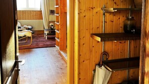 Een houten interieur met een bed, een stoel, een plank met een mand en een opbergende paraplu.