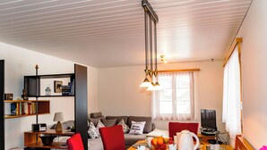 En moderne stue med spiseplads, en sofa, et fjernsyn og en reol.