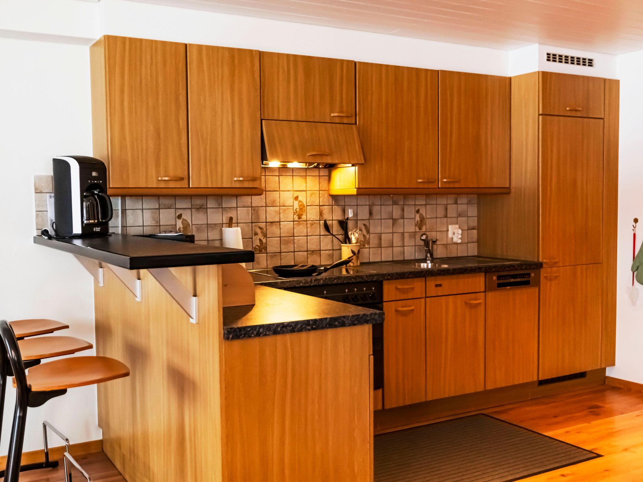 A compact kitchen with wooden cabinets, a coffee maker, a stove, and a small island with bar stools.