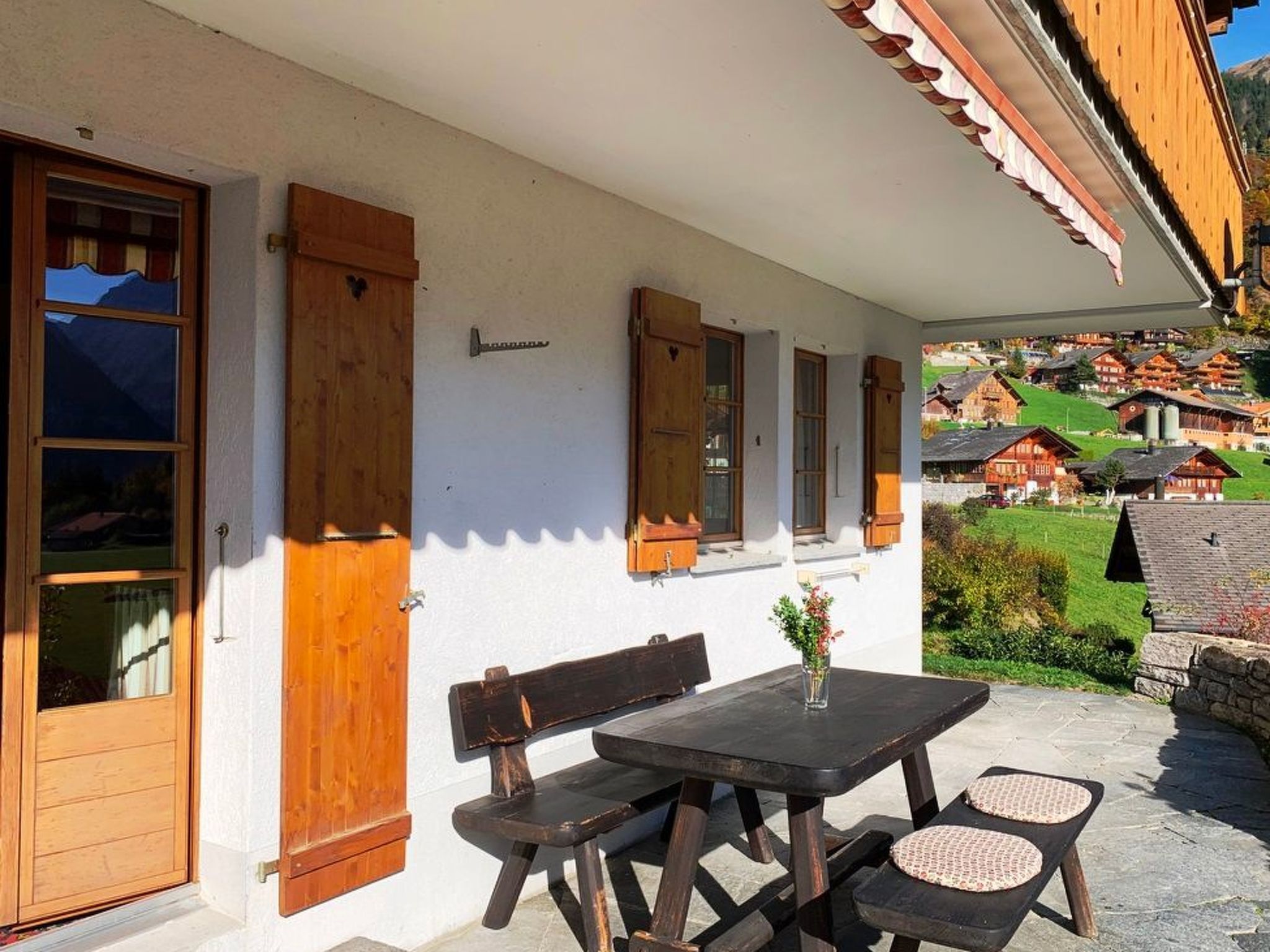 A traditional chalet with wooden shutters, a stone bench, and a table with a vase.