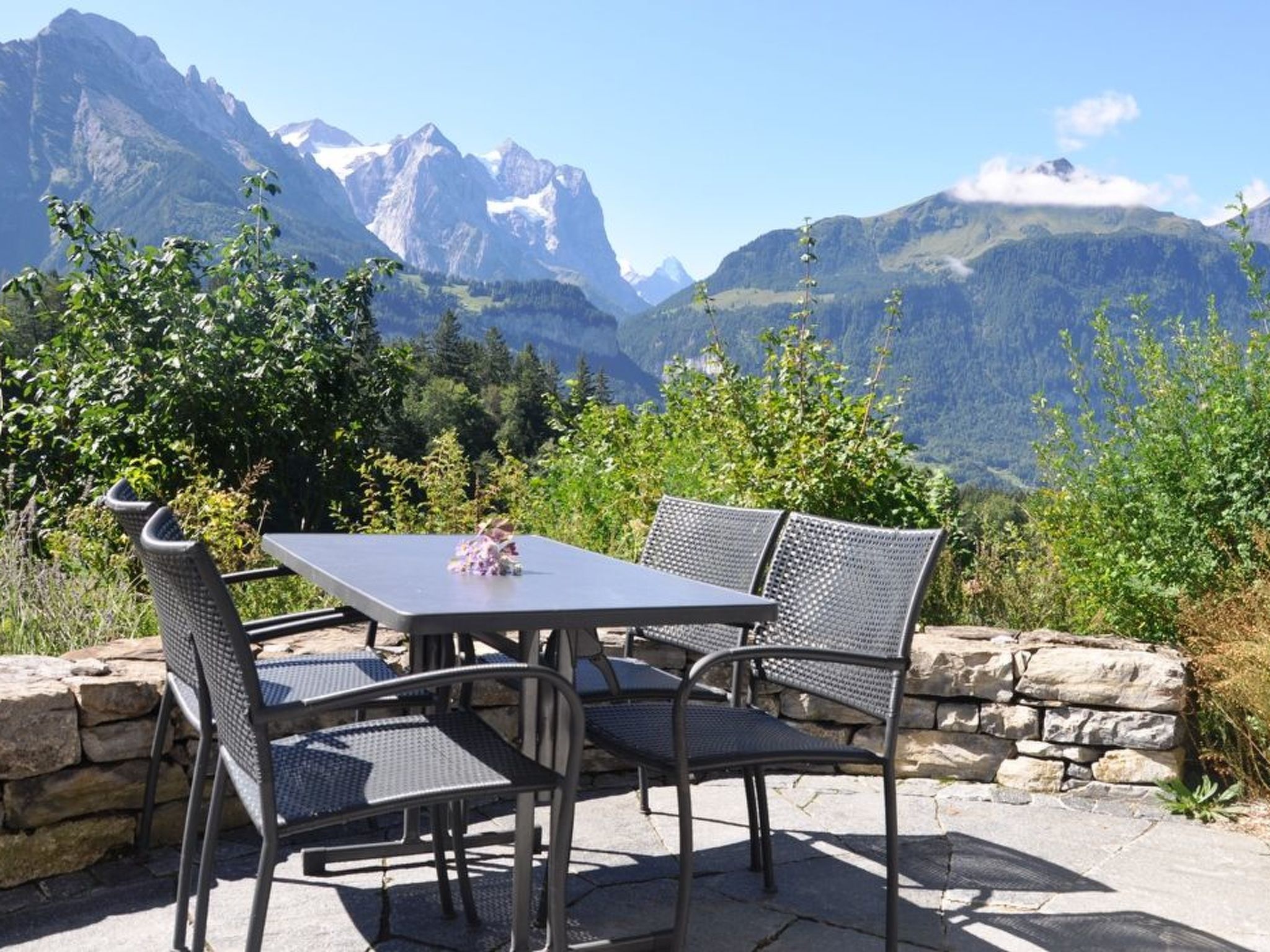 An outdoor seating area with a table and chairs, overlooking a mountainous landscape.