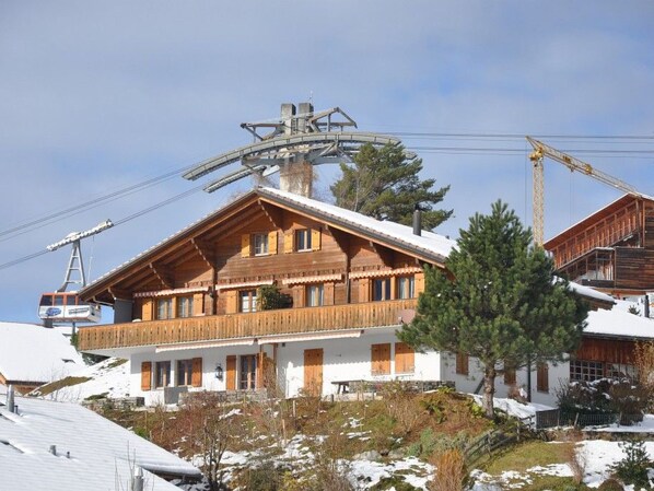 Un chalet in legno con un balcone, una seggiovia sullo sfondo e un paesaggio innevato.
