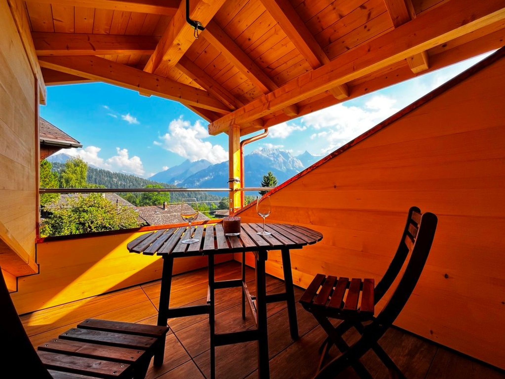 A wooden deck with a table and chairs, overlooking a mountainous landscape.