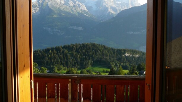 A mountain view from a wooden balcony with a railing.