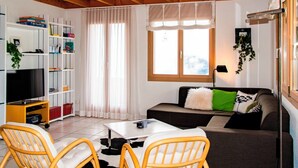 A living room with a TV, sofa, chairs, a coffee table, and a bookshelf.