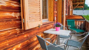 A wooden cabin with a patio area featuring a table and chairs, a potted plant, and a green chair.