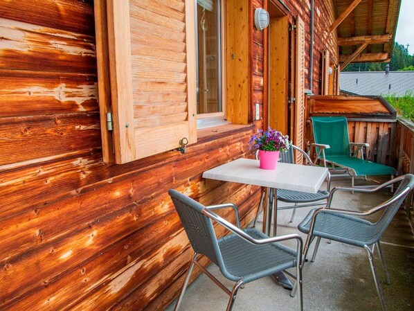Una cabaña de madera con una mesa y sillas afuera, una ventana y una puerta.