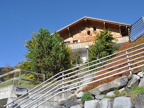 A wooden chalet with a balcony, surrounded by trees and a stone staircase.