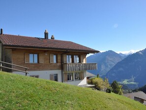 Una casa de dos pisos con un balcón, frente a un paisaje montañoso.