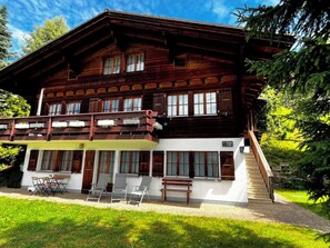 Eine zweistöckige Holzhütte mit Balkon, überdachter Außenbereich und Treppe zum Obergeschoss.