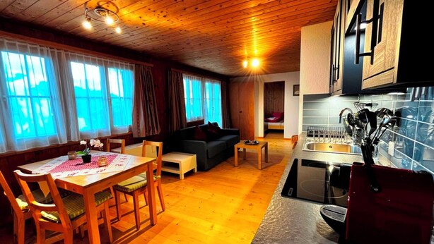Ein gemütlicher Wohnbereich mit Esstisch, Sofa und einer Küche inklusive Spüle und Geschirr.