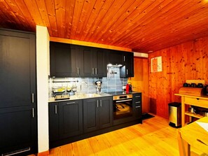Eine Küche mit dunklen Schränken, einem Edelstahlbackofen und einer Holzbalkendecke.