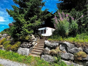 Eine steinerne Treppe führt zu einem weißen Gebäude, das von Grünpflanzen und Bäumen umgeben ist.
