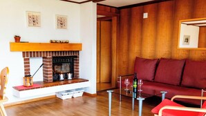 Un salon avec une cheminée, un canapé rouge, une table basse en verre et un plancher en bois.