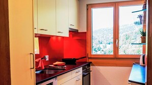 Une cuisine avec des meubles blancs, un plan de travail rouge et une fenêtre donnant sur un paysage enneigé.