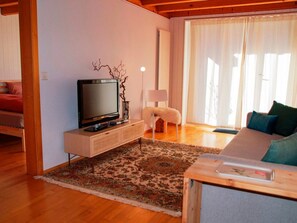 A modern living room with a flat-screen TV on a wooden cabinet, a patterned rug, a white chair, and a sofa with cushions.