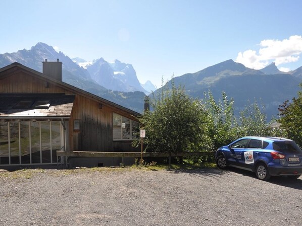 A building with a glass facade, a parked car, and a mountainous backdrop.