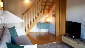 A cozy living room with a wooden staircase, a sofa with cushions, a small side table with a lamp, and a television on a stand. - HasliRent, Wandelhorn 2, (Hasliberg Reuti), by Interhome (Hasliberg)