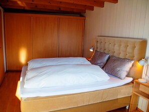 A bedroom with a large bed, wooden wardrobe, and a nightstand with a lamp.