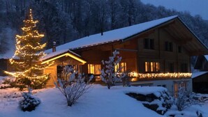 Eine Holzhütte mit schneebedecktem Dach, umgeben von verschneitem Gelände und Bäumen.
