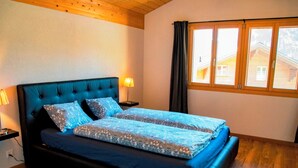 Ein Doppelbett mit dunklem Kopfteil, ein Nachttisch mit Lampe und ein Fenster mit Vorhängen.