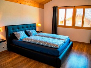 Ein Schlafzimmer mit einem großen Bett, Holzboden, einem Fenster mit Vorhängen und einem Nachttisch mit Lampe.